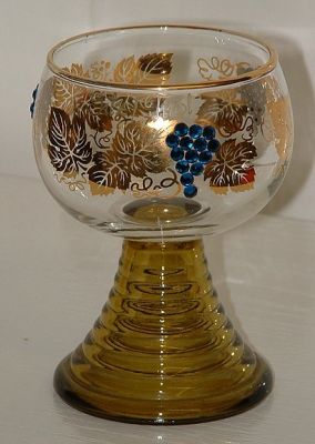 Medium  Roemer
4" tall, decorated with gold vine leaves and applied blue "gemstones" to form the grape bunches. Olive hollow stem open at the base. Has the words Silz / Tirol in gold above the vines on one side of the bowl. Unknown maker.
